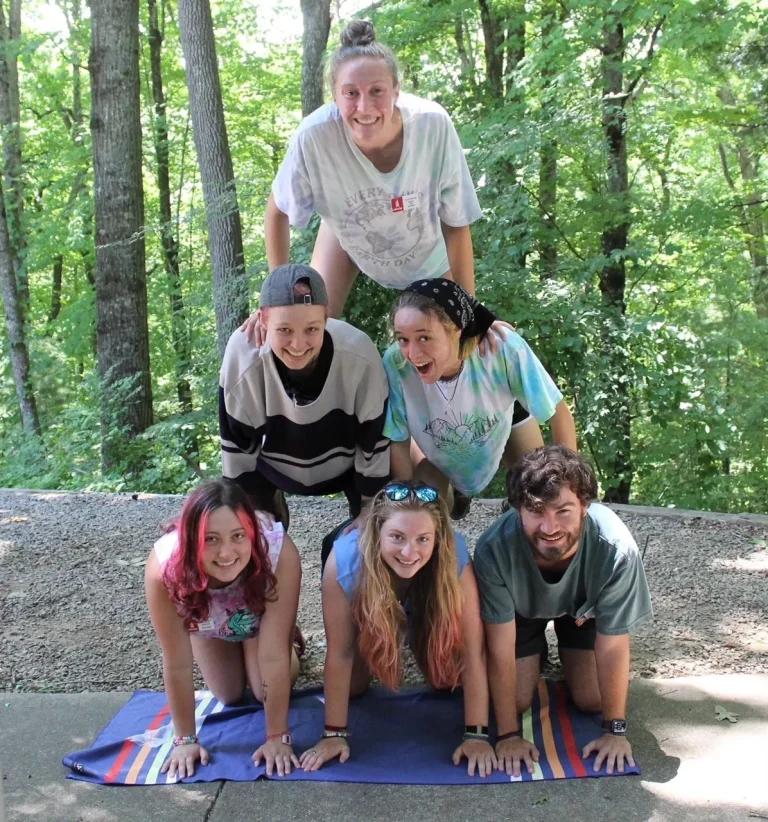 Six Lutheridge summer staff laughing together in a human pyramid in the woods