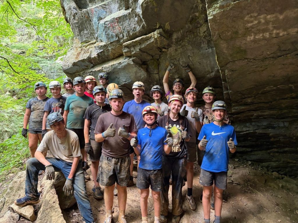 Cave & Wave campers in helmets and muddy clothes giving thumbs up outside the cave