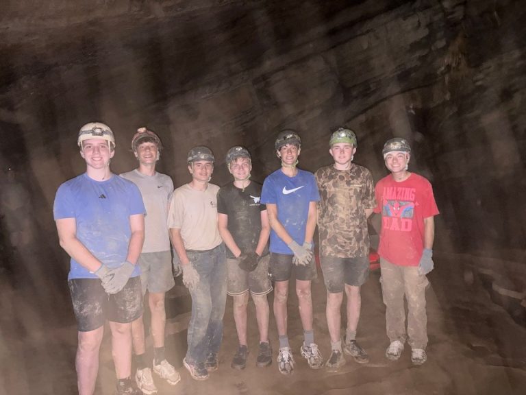 Cave & Wave campers in helmets with headlamps lined up inside the cave