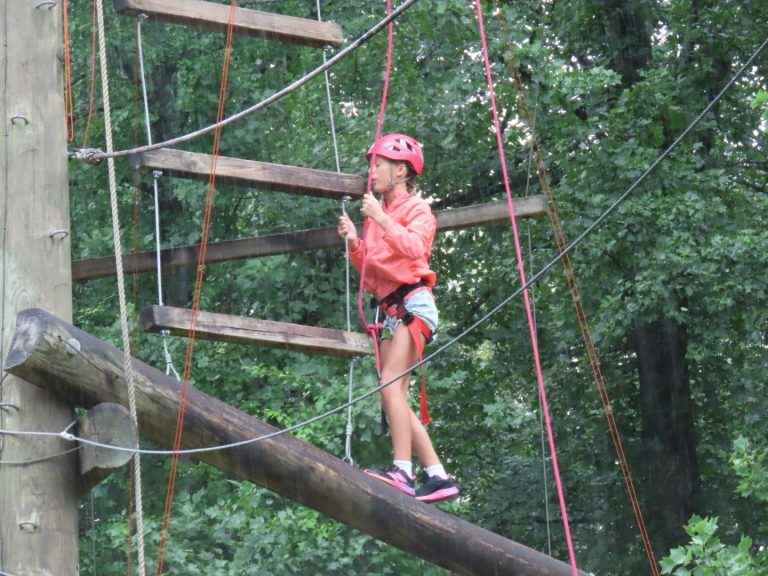A camper in a red helmet crossing a log on the high ropes course