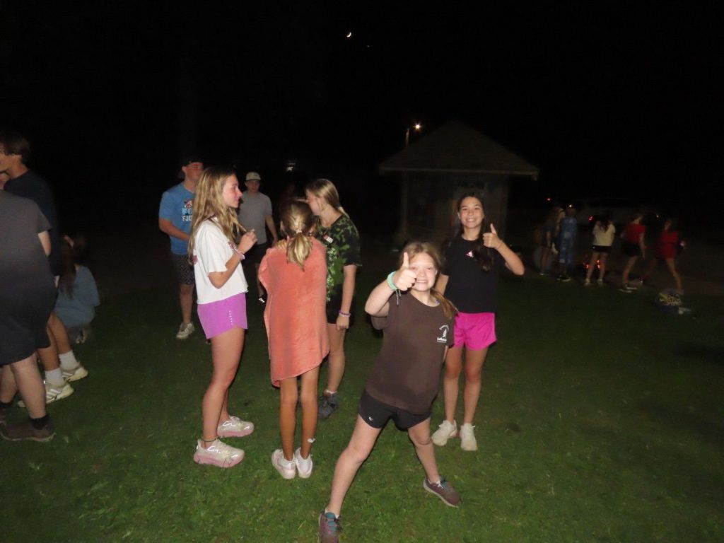 Night Owl campers out on the field after dark, one giving a thumbs up