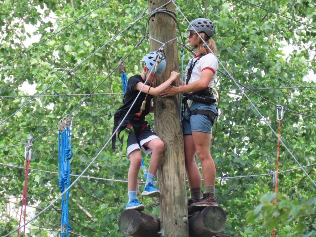 A counselor helping a camper up the pole on the high ropes course