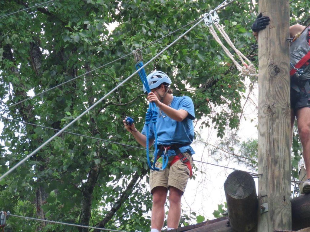 A camper in a helmet and harness clipped in on the high ropes course