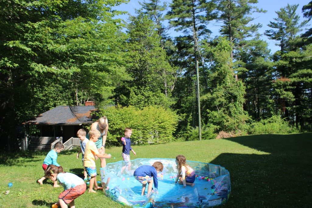 PreKamp campers splashing around a kiddie pool on the lawn on water day
