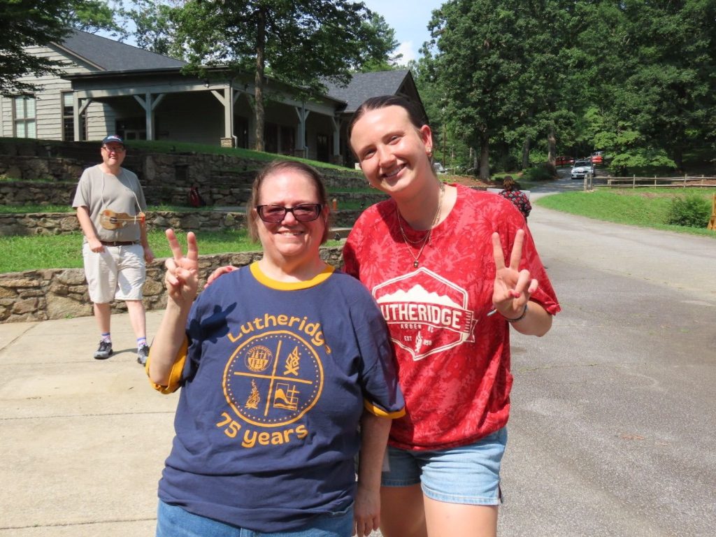 A Summershine camper in a Lutheridge 75 years shirt and her counselor giving peace signs